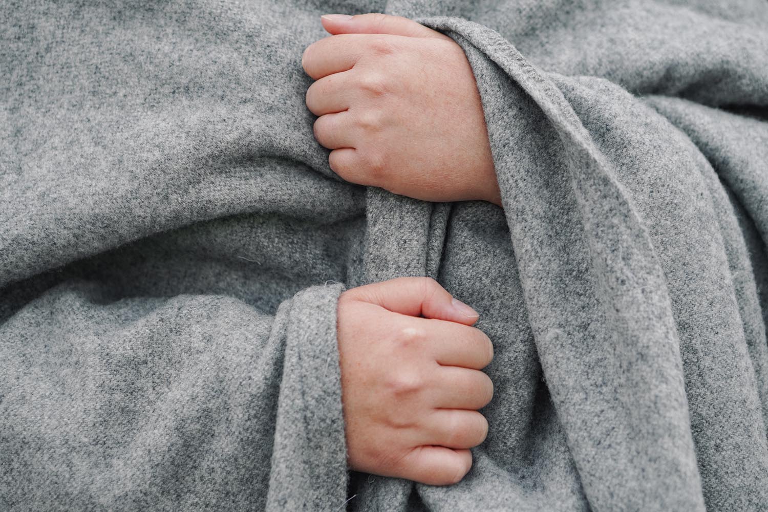 Close up of a person wrapped in a grey blanket with their hands holding the blanket closed