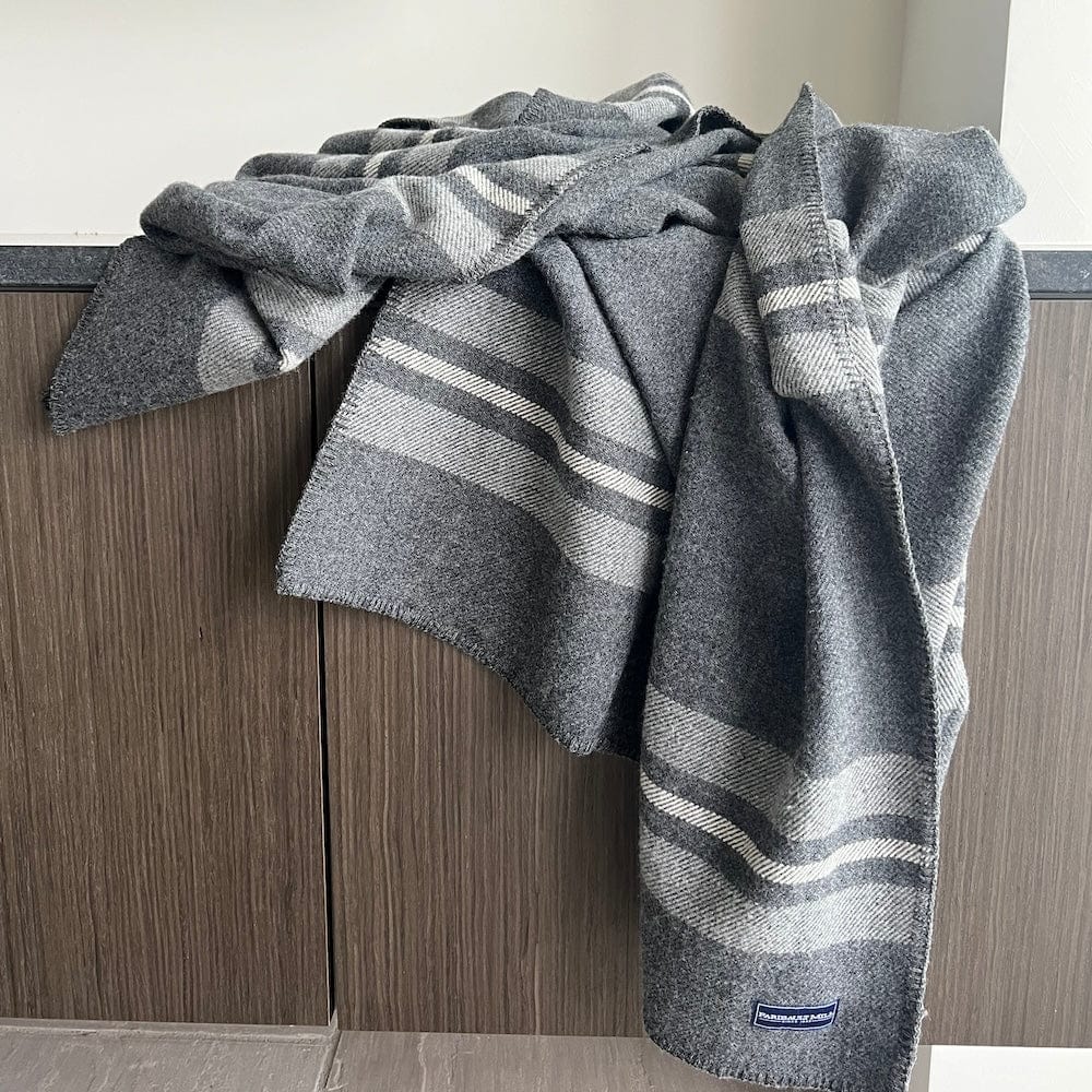 Cabin throw wool blanket in charcoal with heather gray and natural stripes draped over a dark wood cabinet in a modern lifestyle setting.