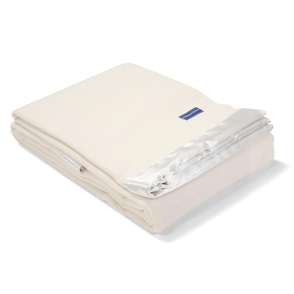 Faribault Mill Pure and Simple Satin bone white middleweight wool bed blanket, folded and displayed at an angle to highlight the thickness, loft of the wool, and satin edges.