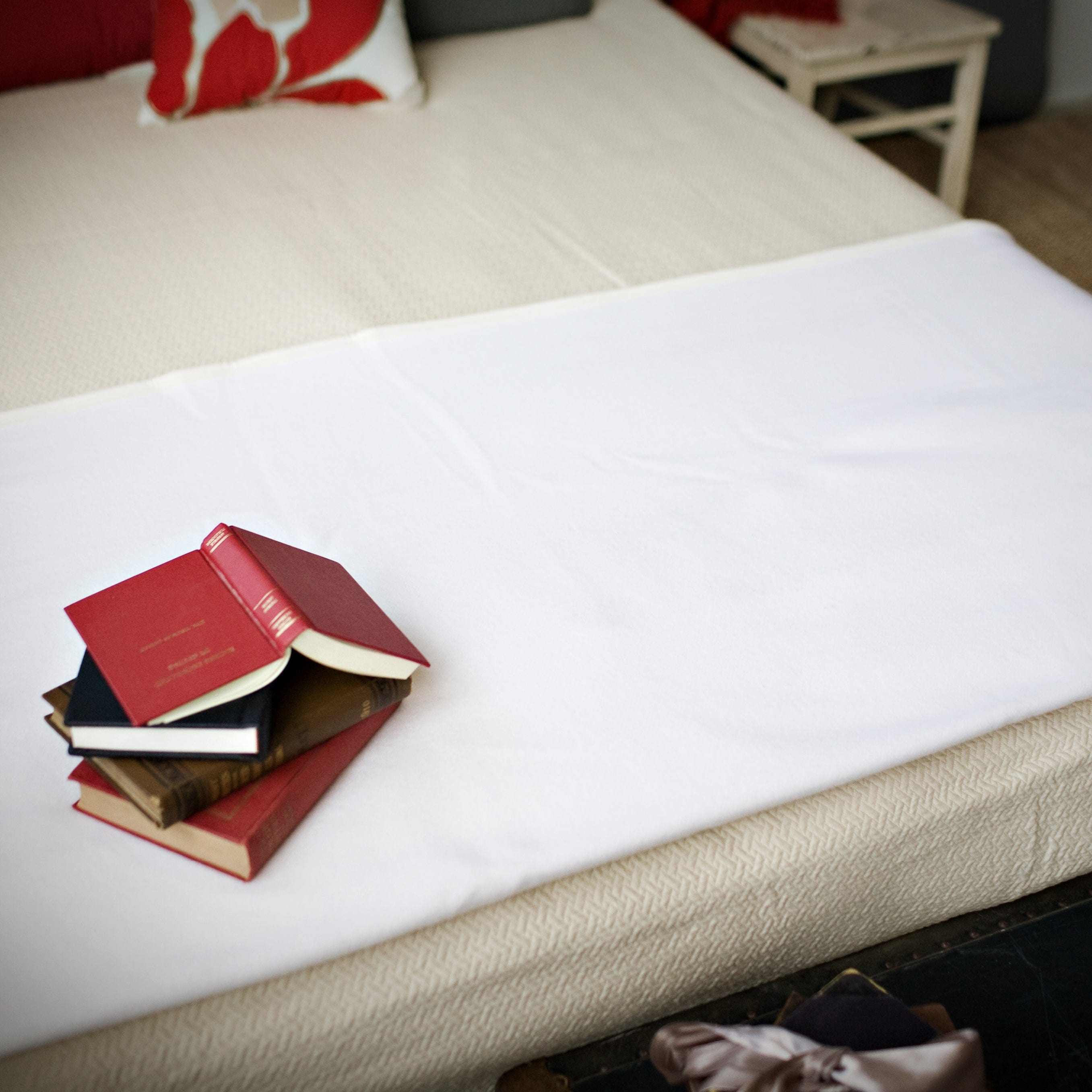 Pure and Simple Bone White middleweight wool blanket laid flat across a bed, styled with a small stack of books featuring a prominent red cover.
